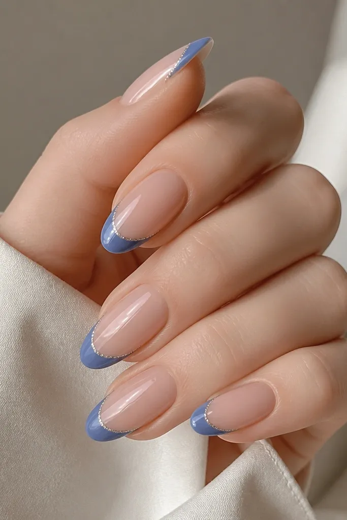 Almond nails with nude base; medium blue French tips; a dotted glitter line runs inside the blue near the smile curve; glossy finish.