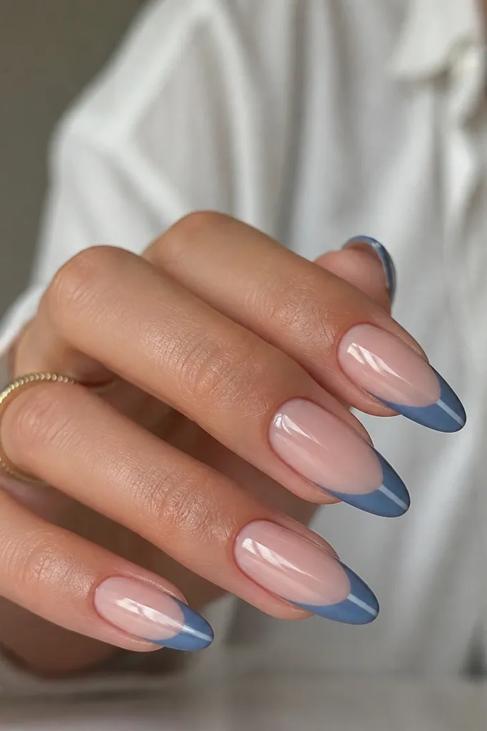 Almond nails with nude base; blue French tips that are mostly matte or satin, plus one glossy vertical stripe through the tip area on each nail; glossy finish overall but stripe stands out.