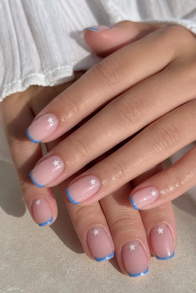 Medium squoval nails with sheer pink base. Blue French tips are narrow. A tiny white five-point star sits near the cuticle on one side of each nail.