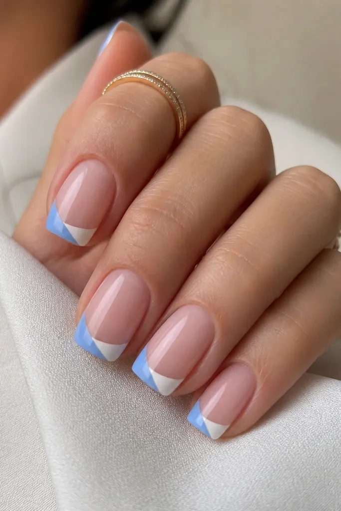 Soft square nails with sheer nude base. The French tip is split diagonally: blue on one side and white on the other, meeting at a clean diagonal line.