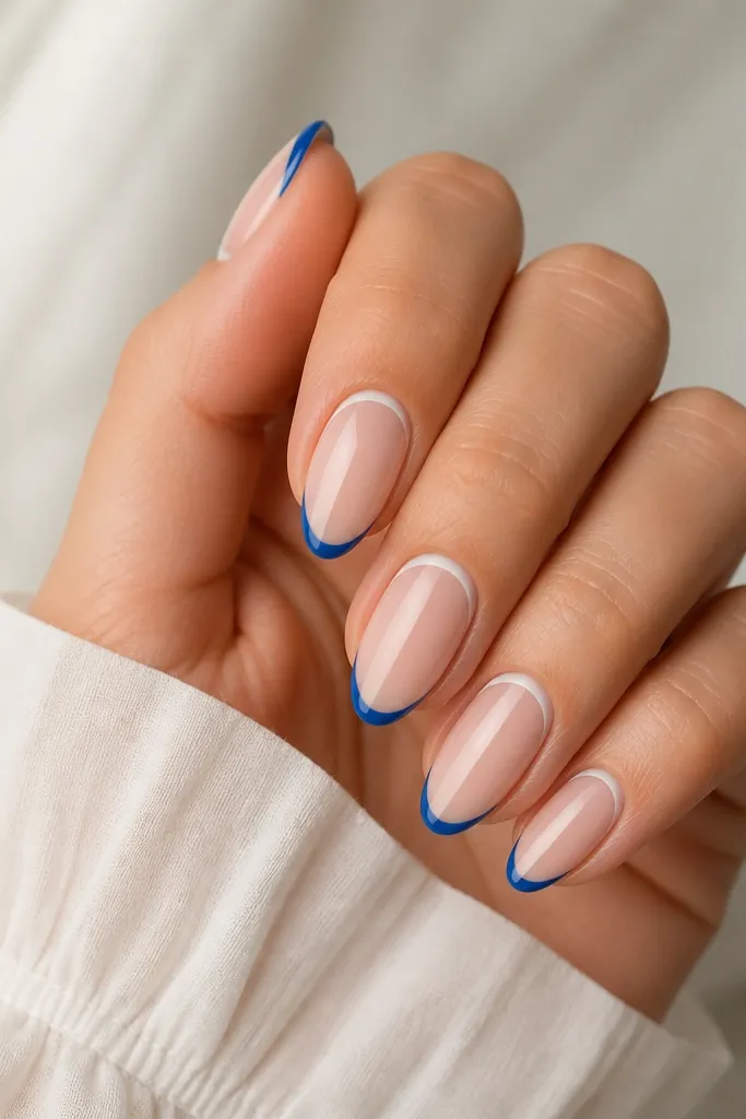 Medium almond nails with sheer nude base. Blue French tips are narrow. A thin white line runs under the cuticle in a curved halo, not touching the side walls.
