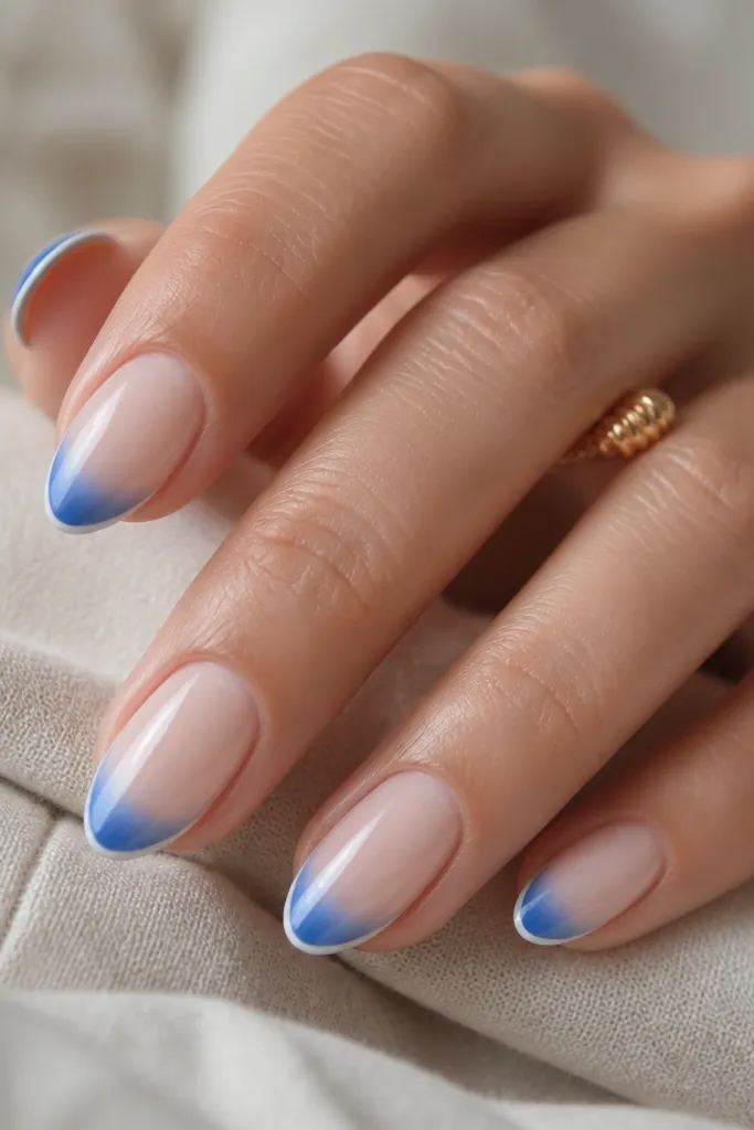 Short almond nails with sheer nude base. The tips fade from deep blue at the outer edge to lighter blue near the center, with a thin white fade line at the very edge.