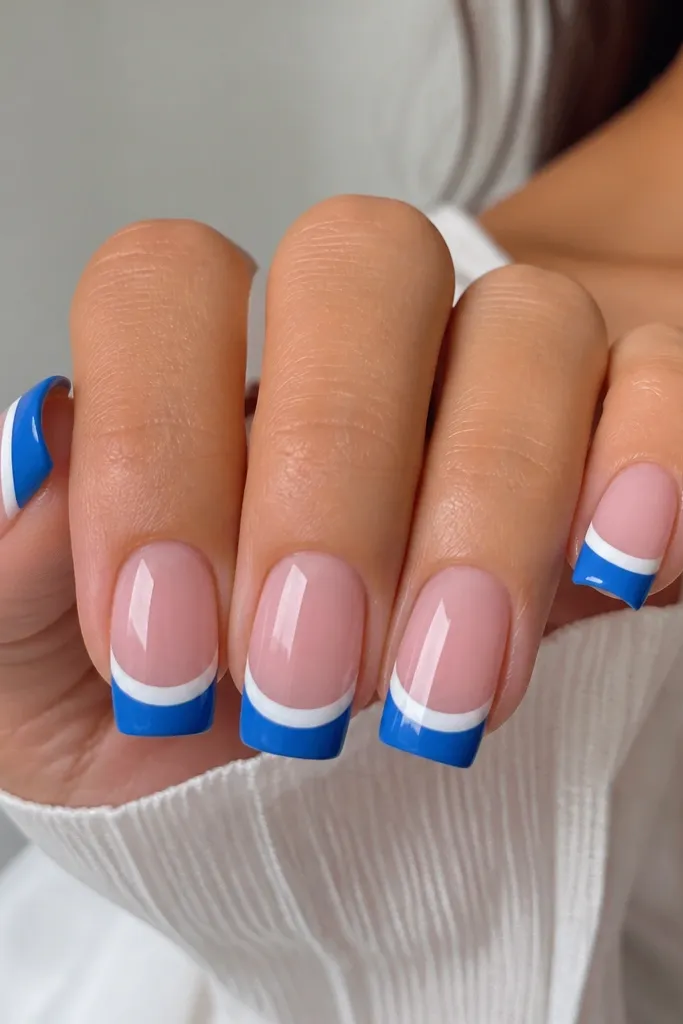 Medium square nails with a translucent pink base. The blue French tips are solid and the smile line has a thicker white stripe running across, like a bold arc. Glossy finish, clean edges.