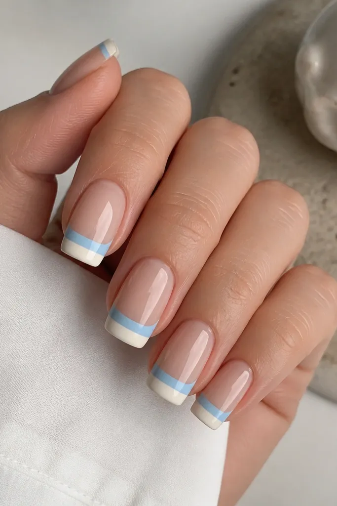 Medium square nails with a nude base. The French tip is split horizontally: the upper half is soft blue, the lower half is creamy white. The split line is straight and crisp.