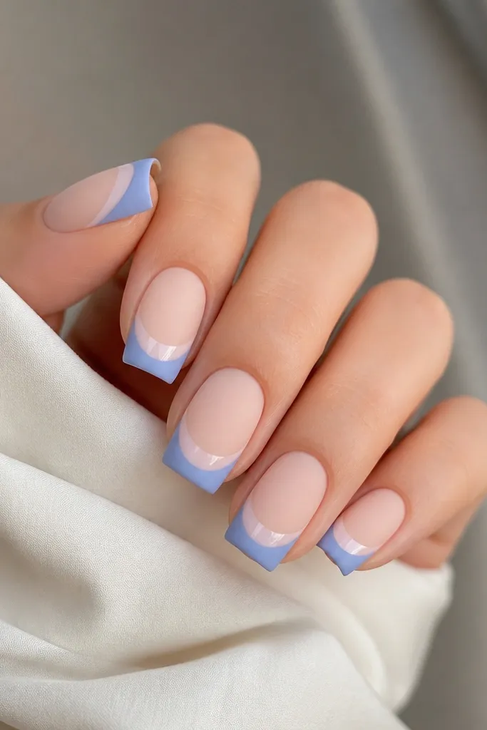 Square nails with a nude base. French tips are matte periwinkle. On each tip, there's a glossy milky white arc just above the smile line, creating a shine contrast. Matte overall with a glossy arc detail.