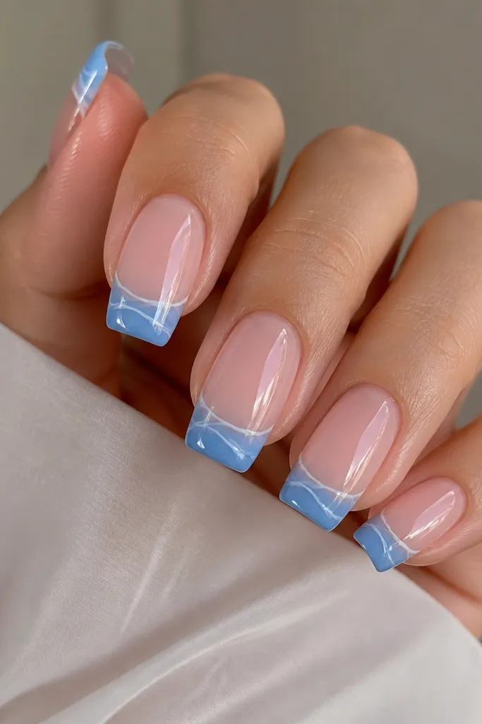 Square nails in a clear jelly base with slight pink tint. Blue French tips are semi-opaque. Each tip has a thin milky white swirl that curves along the smile line. The finish is glossy and jelly-like.