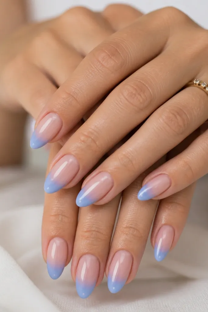 Medium almond nails with a sheer nude base, a soft periwinkle French fade that blends upward like a cloud, and a tiny clear sparkle at the center of each tip.