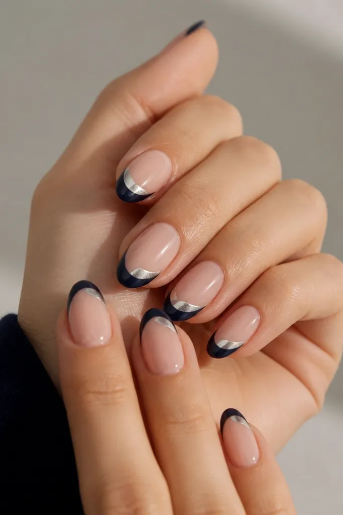 Medium almond nails with navy French tips and a silver foil half-moon on the center of each tip, like a metallic crescent.