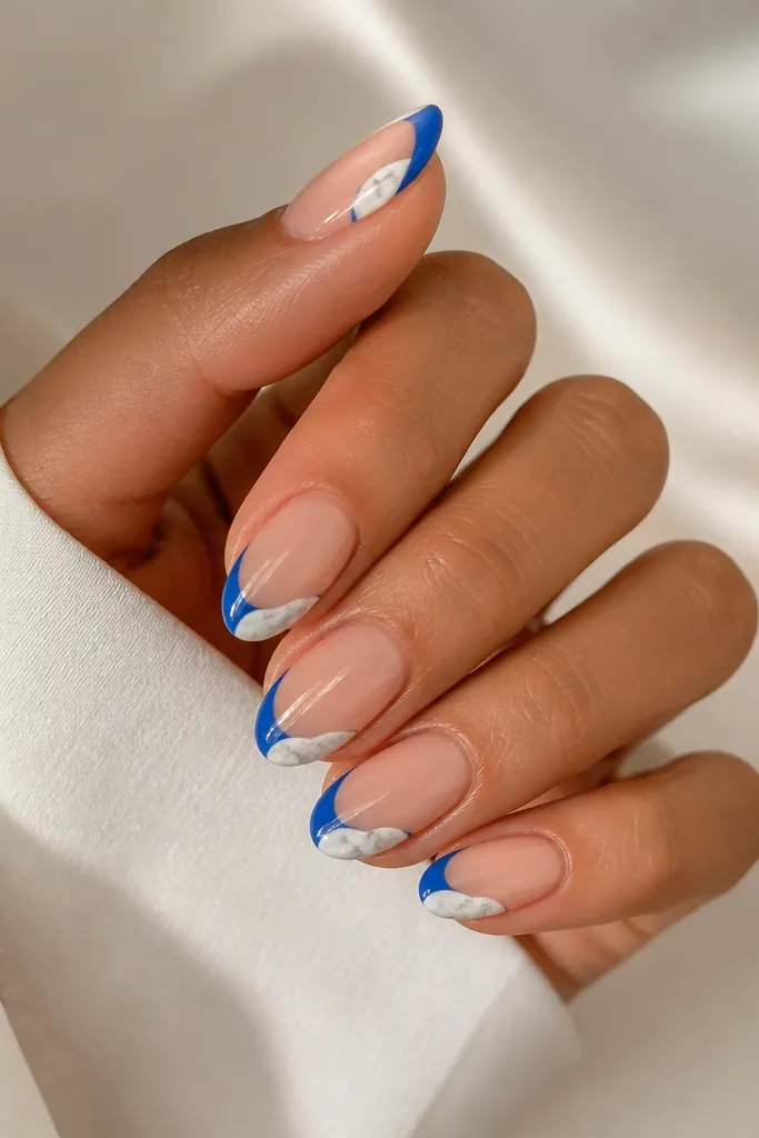 Medium almond nails with blue French tips; each nail has a small white marble patch on the outer corner with gray veining.