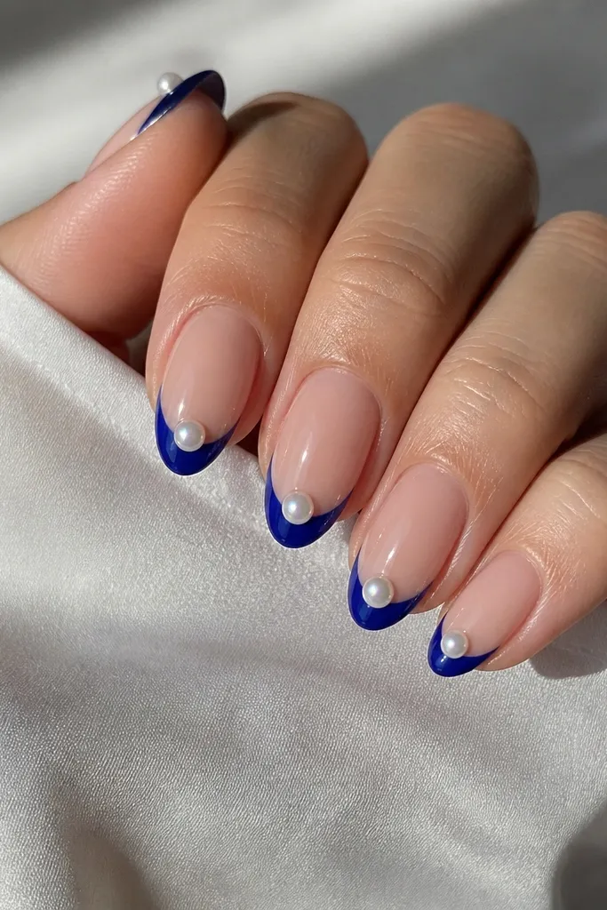 Medium almond nails with royal-blue French tips and a single tiny iridescent pearl placed right on the French edge on each nail.