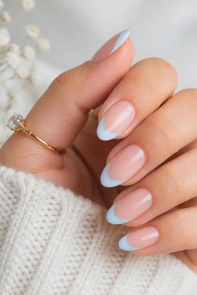 Medium almond nails with ice-blue French tips; the very tip edge has a dusting of fine silver micro glitter like a frost line.