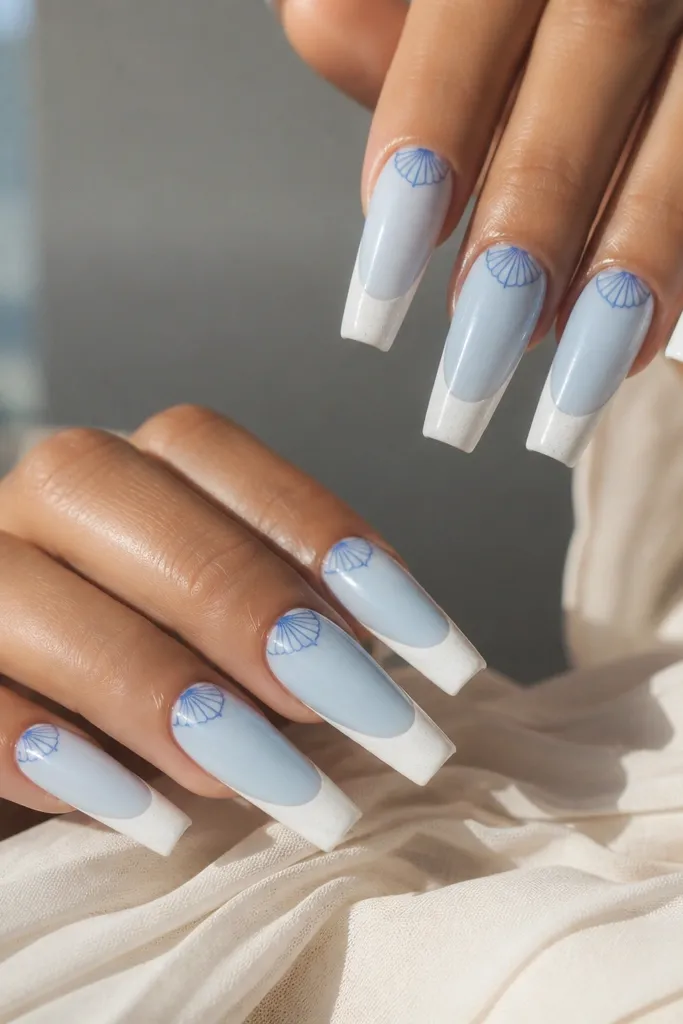 Long coffin nails with soft white foam French tips. The nail beds are pale blue, and each nail has a half-moon shell motif near the cuticle with thin darker blue lines.