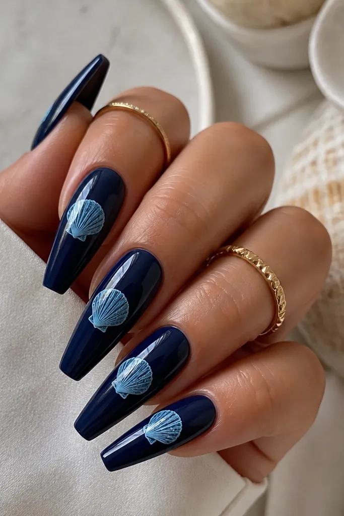 Long coffin nails in deep navy. Each has a shell drawn in ice blue with a thin white highlight line and a glossy top coat.