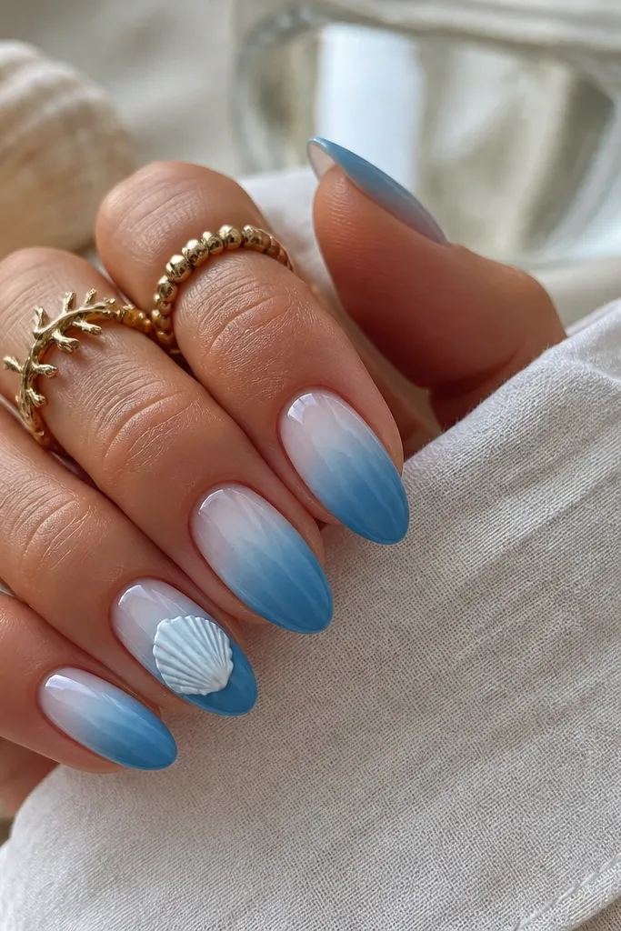 All nails have a blue ombre from pale at cuticle to deeper at tip. The ring finger has a centered white shell with ridges, while other nails are plain ombre with glossy finish.