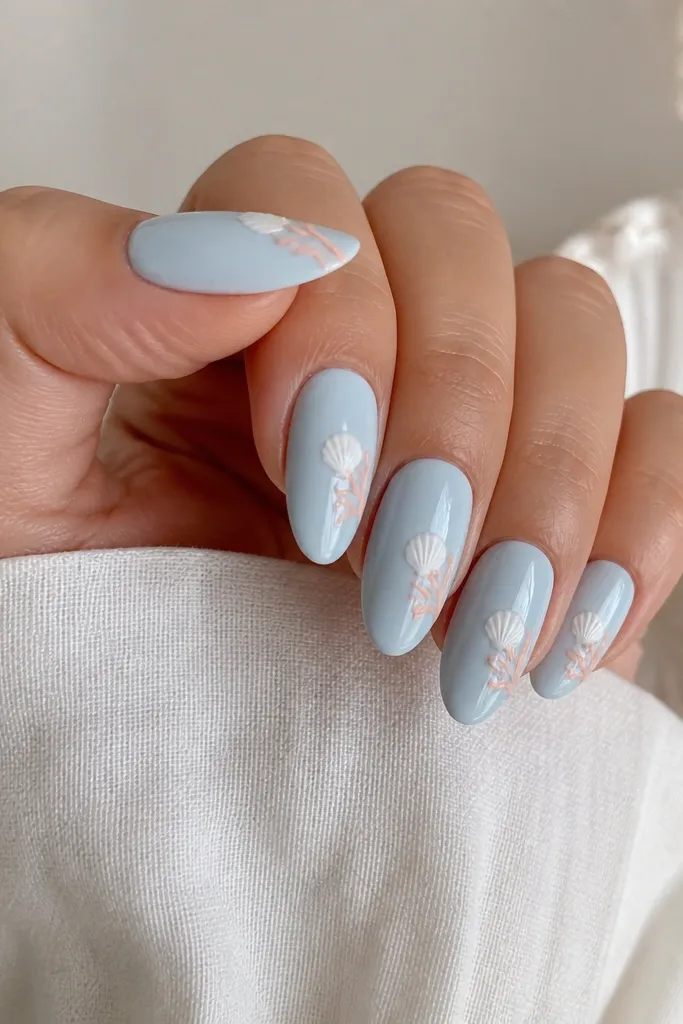 Almond nails in pale blue. A white shell is centered, and along one side of the shell there are tiny peach corral-like curved lines with glossy finish.