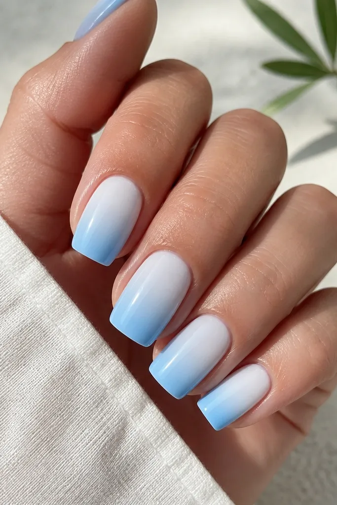 Five square nails with a smooth gradient from milky white at the cuticle into icy sky blue toward the tip. Edges are straight and corners look gently softened. The finish is glossy and reflects sunlight.