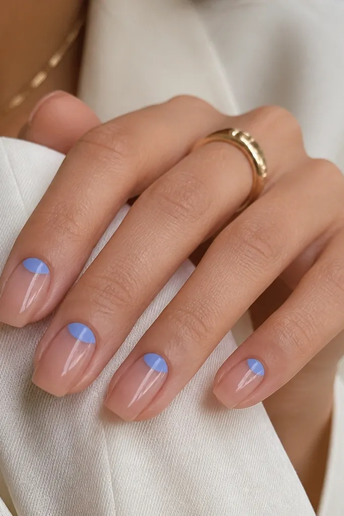 Square nails in a sheer nude base. Half-moon shapes near the cuticle are painted in periwinkle blue, leaving the rest of the nail transparent and glossy. The half-moons are crisp and slightly rounded.