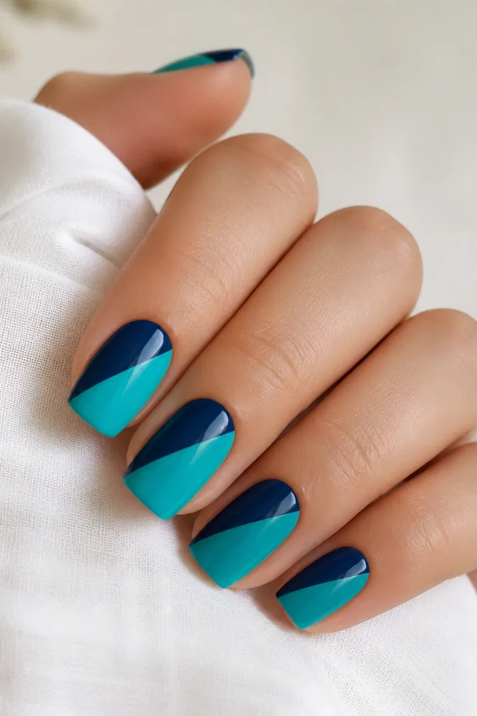 Square nails with a split diagonal design: navy blue on one triangle and turquoise on the other. The diagonal line is straight and centered on each nail. Finish is glossy.