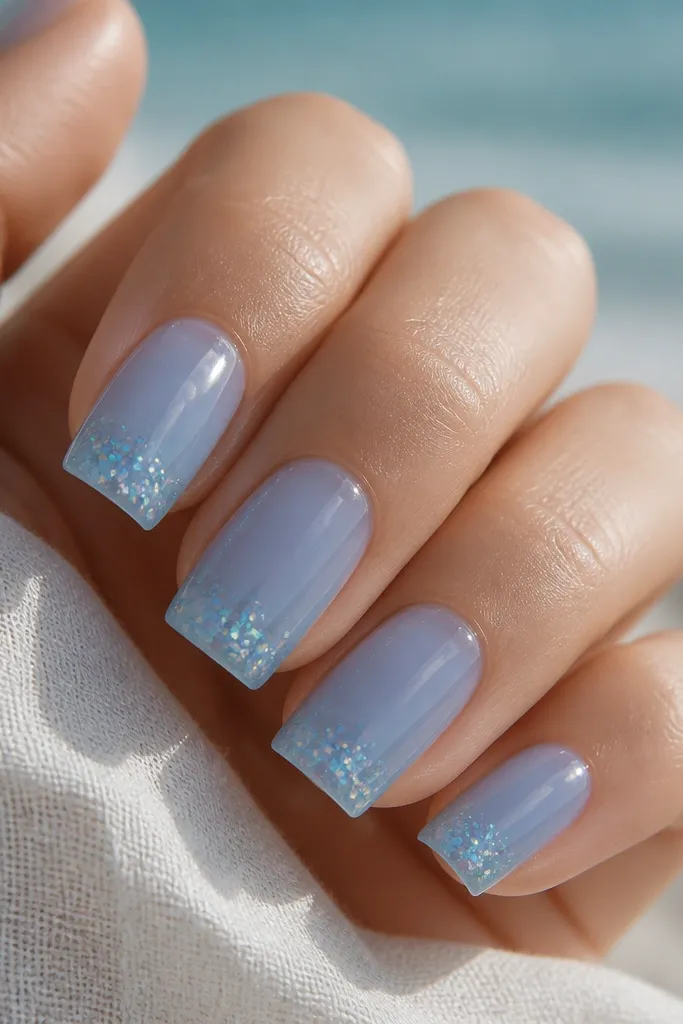 Square nails in a translucent beach-glass blue. There are tiny holographic glitter specks concentrated near the tip. The nails look slightly jelly-like and glossy.