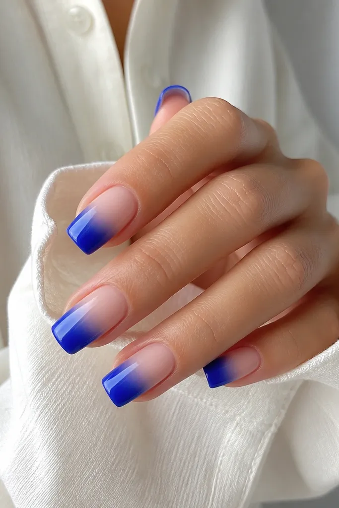 Square nails with a clear nude cuticle area. The blue ombré starts around mid-nail and fades to deeper royal blue at the tip. Glossy finish.