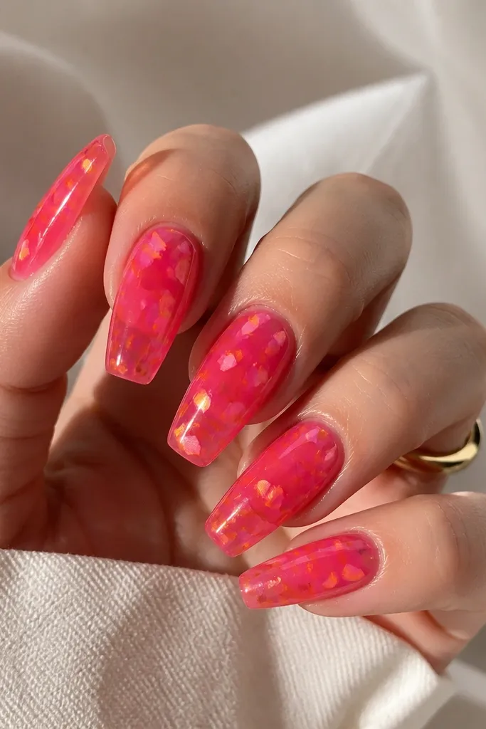 Medium coffin nails with a glossy jelly hot pink base that looks slightly see-through. Over it, there are small orange "shards" and confetti pieces scattered randomly, like broken glass.