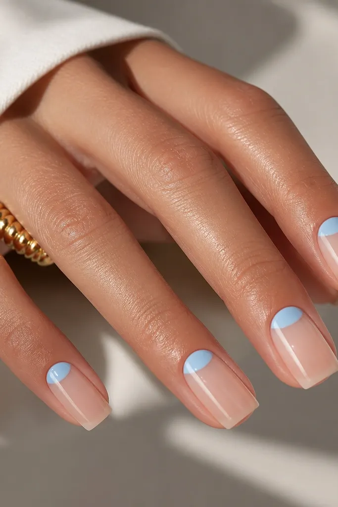 Square nails with a sheer nude base. A sky-blue half-moon sits at the cuticle area on each nail, leaving the rest of the nail clear and glossy. Clean negative space around the sidewalls.