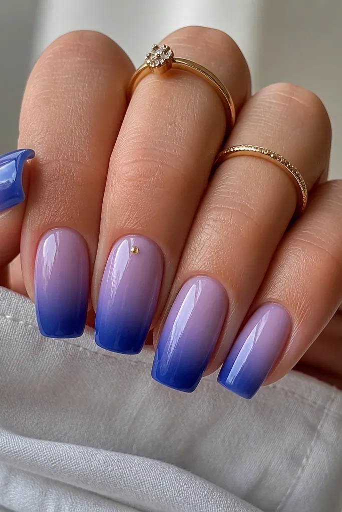 Square nails fade from sheer lilac at the base to deep blue at the tip. On one nail, a tiny gold dot sits near the cuticle. Glossy finish, smooth gradient.