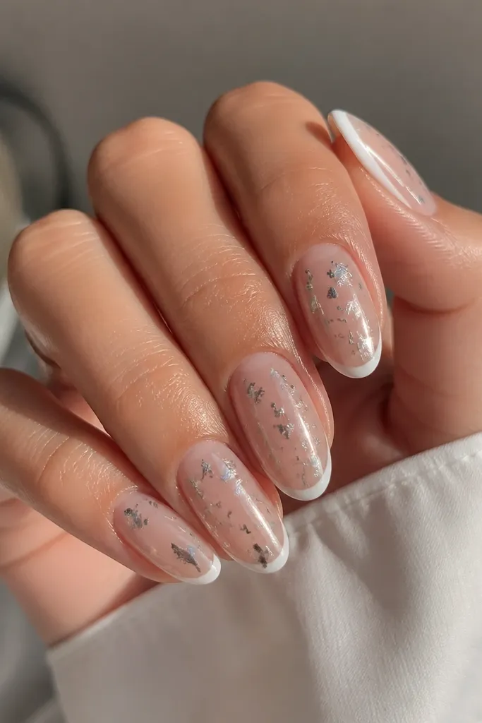 Clear/natural-looking base nails with thin white French tips; instead of full chrome, there are floating chrome flecks and small mirror patches over the nail surface.