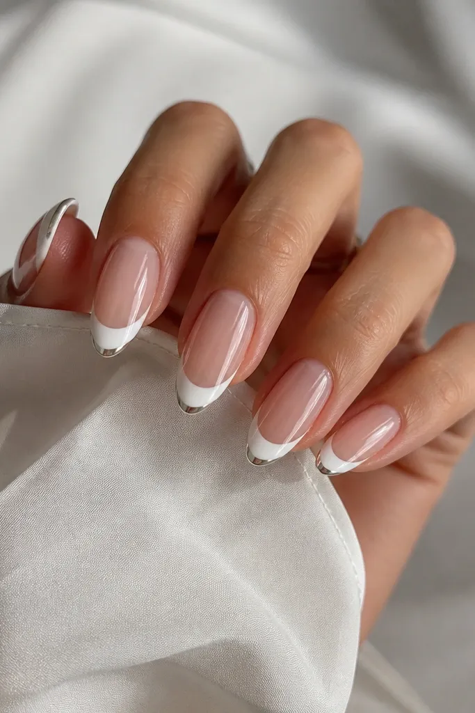 Medium almond nails with a white French tip that turns into a chrome mirror only at the very tip edge; the rest of the nail is clear gloss.