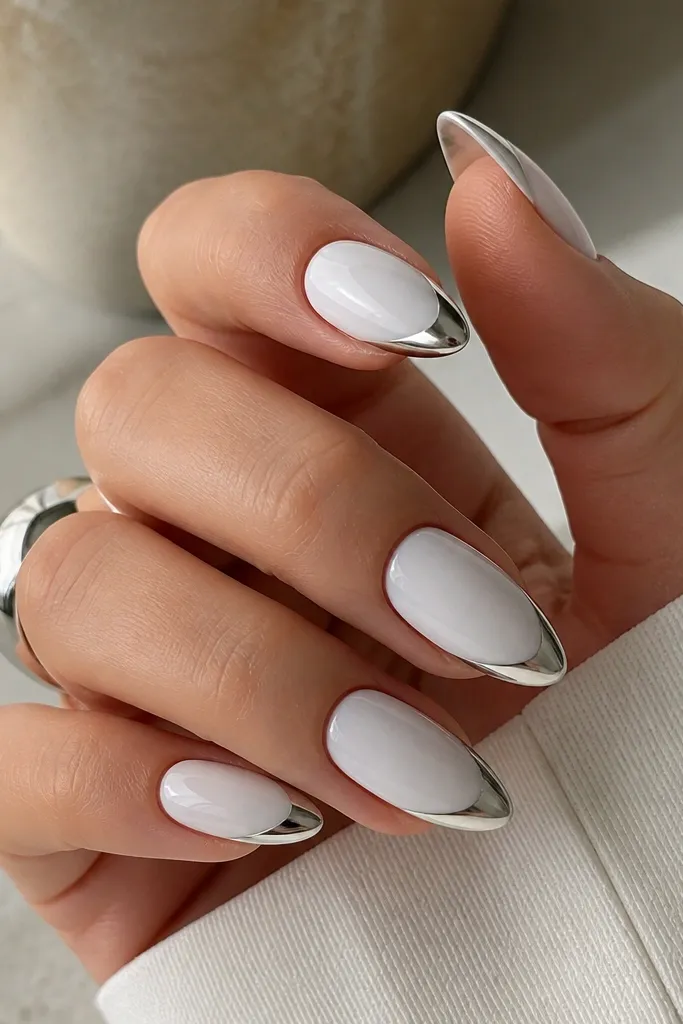 Almond nails with an opaque white base. The French line is an icy silver chrome with a mirror shine, sharply arced near the tip.