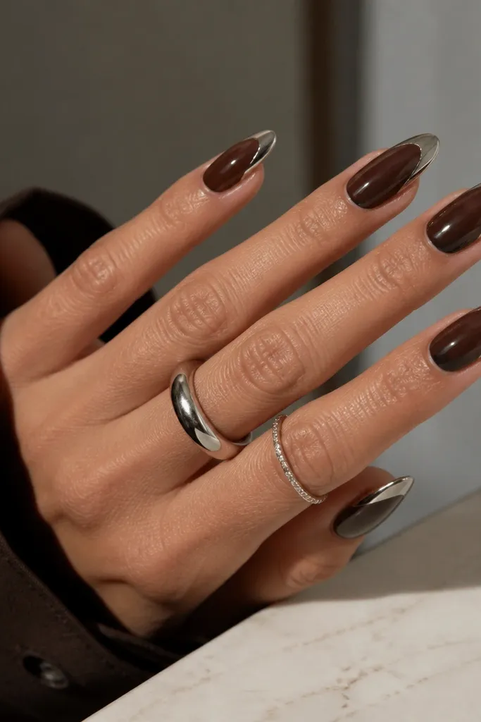 Almond nails with a deep mocha brown base. The French arc is silver chrome, and there is a small negative space window in the center of the French area.