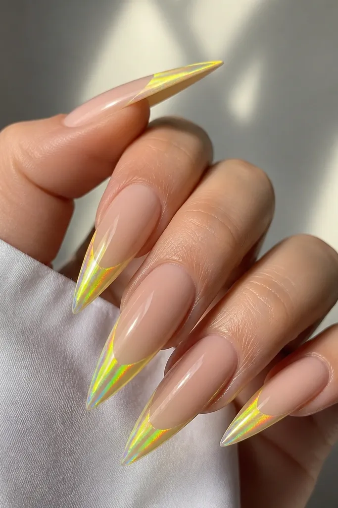 Long stiletto nails with neon yellow French tips. Over the tips, a holographic chrome layer creates rainbow flashes. Nude base, glossy.