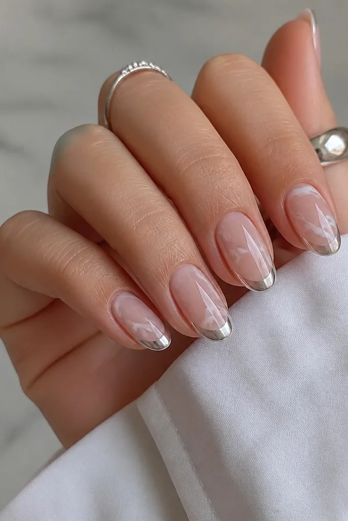 Medium oval nails with white marble swirls on a nude base and a silver chrome French tip with a thin vein-like shine.