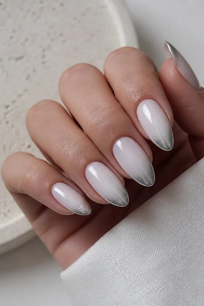 Almond nails with a milky white base. The French tip has silver chrome that fades into the milky white, creating a soft gradient band. The smile line is clean and slightly higher at the center.