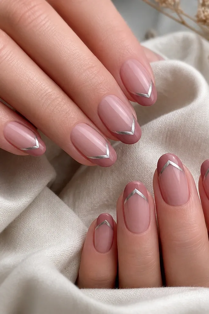 Short almond nails with a dusty rose base. The French tip is a matte dusty rose band, and in the center of the band there's a mirror silver chrome chevron pointing down toward the tip edge. The chevron is small and crisp.