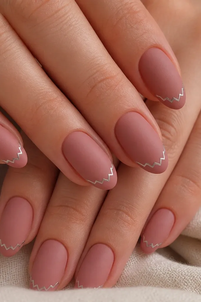 Short almond nails with a dusty rose base and a matte dusty rose French band. Along the center of the French band there's a tiny mirror silver zigzag line, like a miniature lightning bolt, with sharp edges.