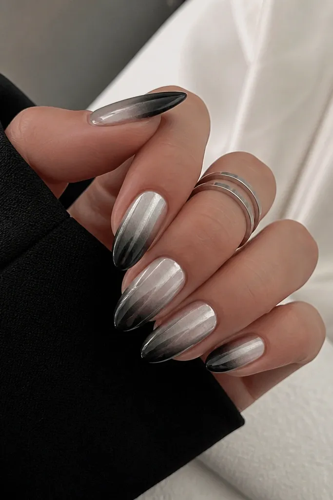 Medium almond nails with a glossy black tip that fades upward into a lighter, smoky grey gradient. The fade transitions into a silver chrome effect around the outer half of the nail, blending smoothly.