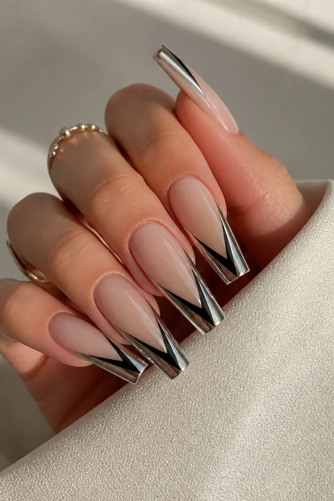 Long coffin nails with a sheer nude base. The French tip is a black V-shaped notch in the center, surrounded by mirror silver chrome on both sides of the tip. The V notch is clean negative space down the middle.