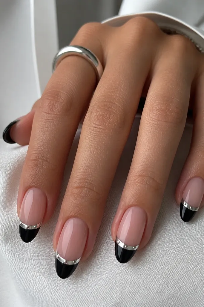 Medium almond nails with black tips in a French shape. The French smile is chrome mirror silver, and three tiny flat-back silver studs sit evenly across each smile line.