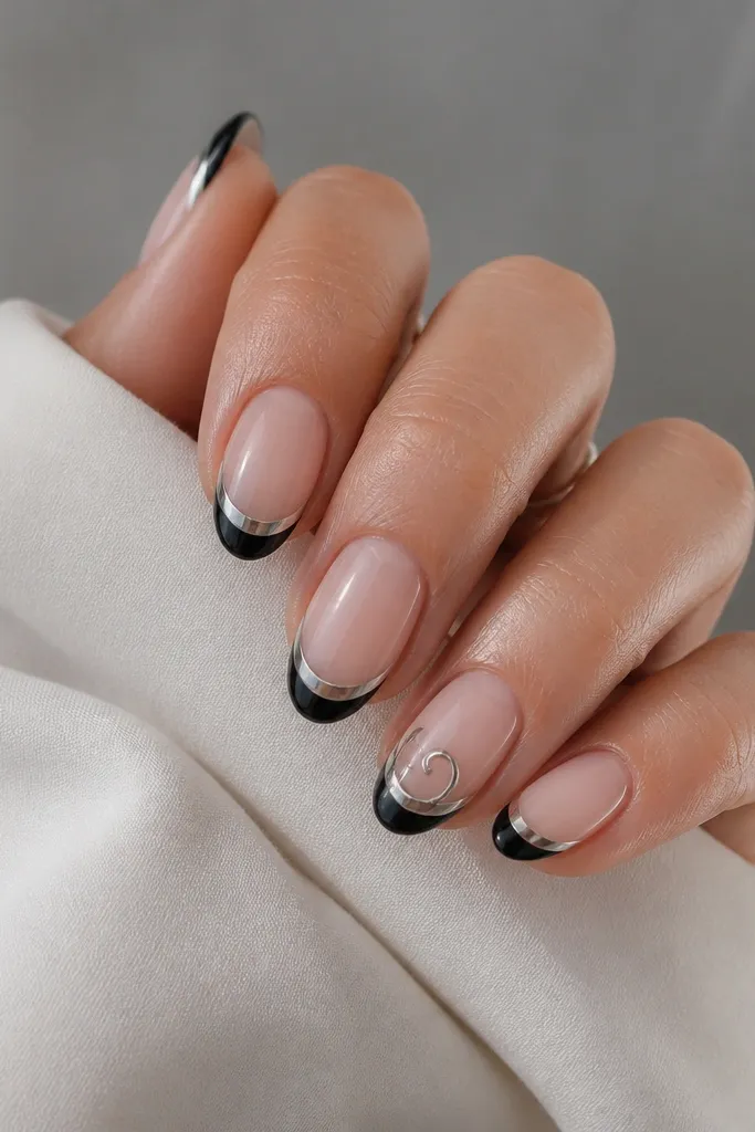 Four nails have a clean black French tip with mirror silver chrome on the smile. The ring finger has an added chrome swirl tail that curls from the smile toward the center, like a tiny signature.