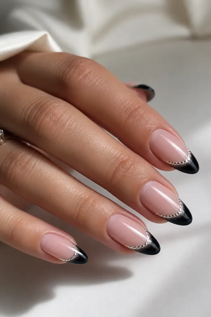 Long almond nails with black French tips. The smile line has a mirror chrome "lace edge" made from tiny connected dots and short brush strokes, creating a delicate scalloped border.