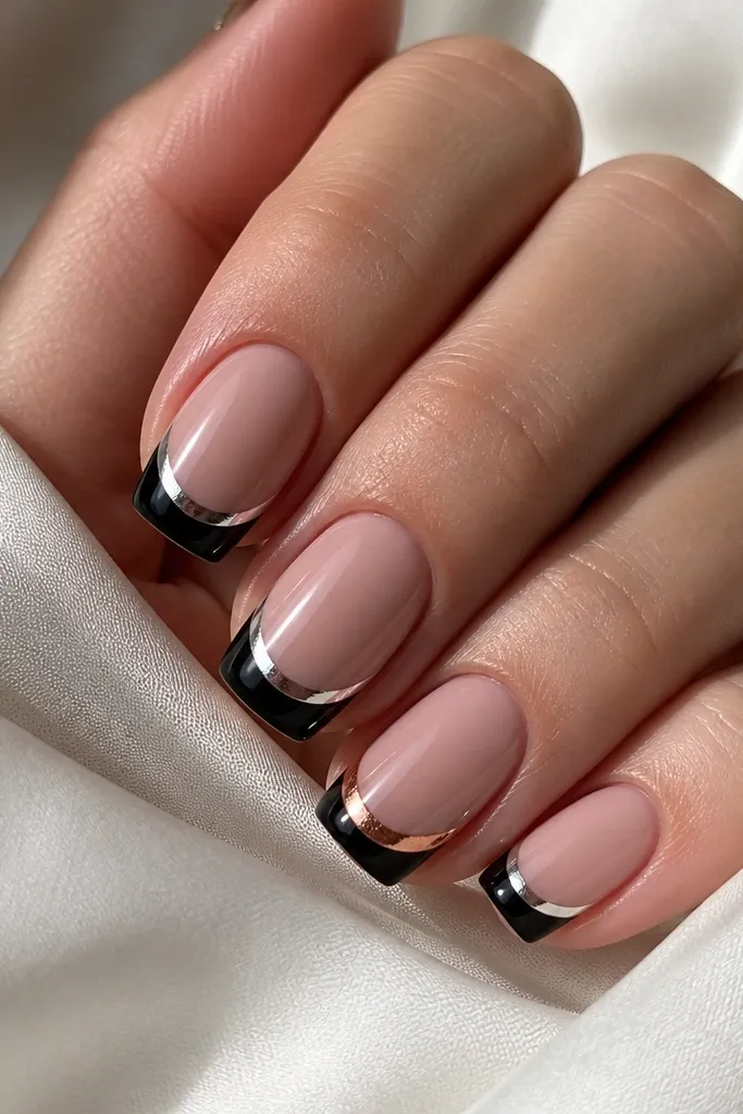 Four nails show glossy black French tips with mirror silver chrome smile lines. The ring finger has the same setup, but the smile line is rose-tinted chrome, giving a soft pink-gold reflection.