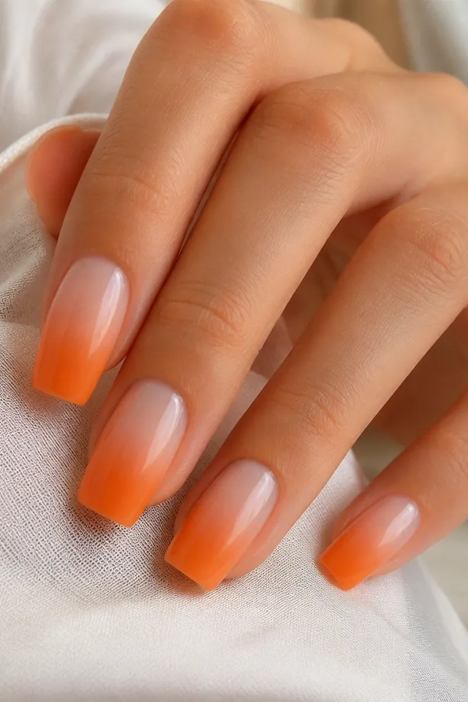Square nails with a smooth ombre that fades from tangerine at the tip into nude near the cuticle; the blend looks airbrushed and glossy.
