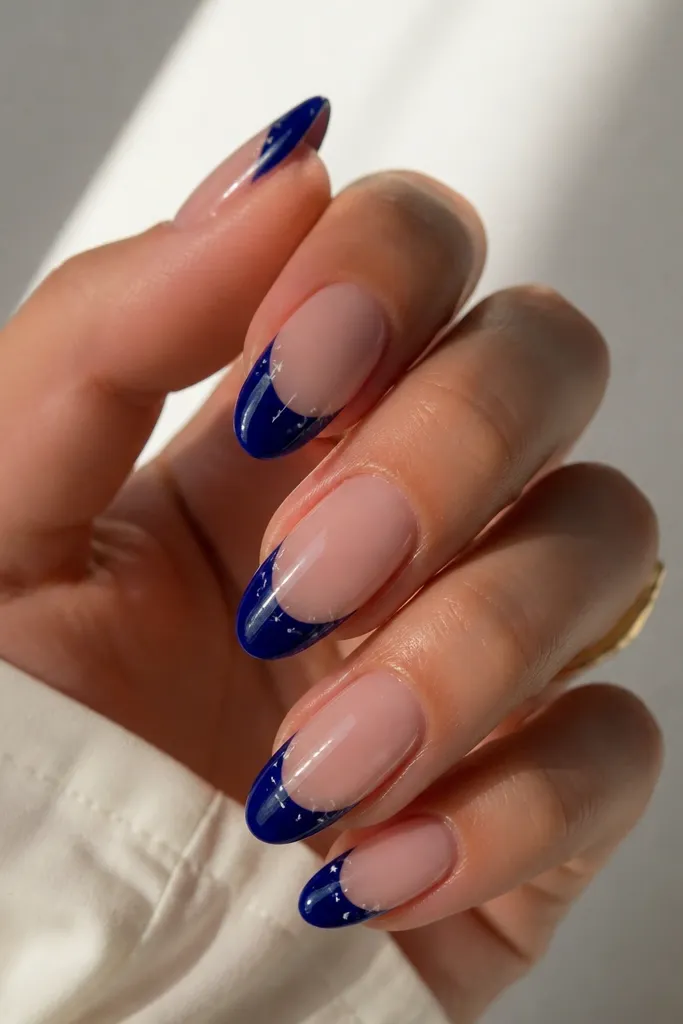 Almond nails with deep blue French tips and tiny white star dots scattered near the smile line, glossy finish.