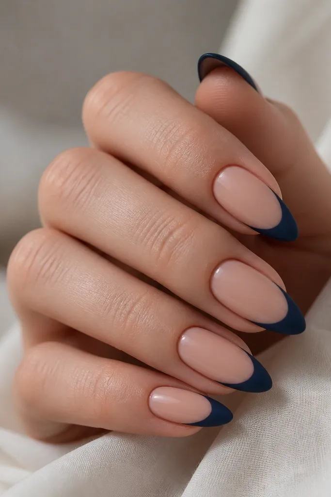 Almond nails with nude base; navy French tips are matte, while a thin glossy clear line follows the smile line for contrast.
