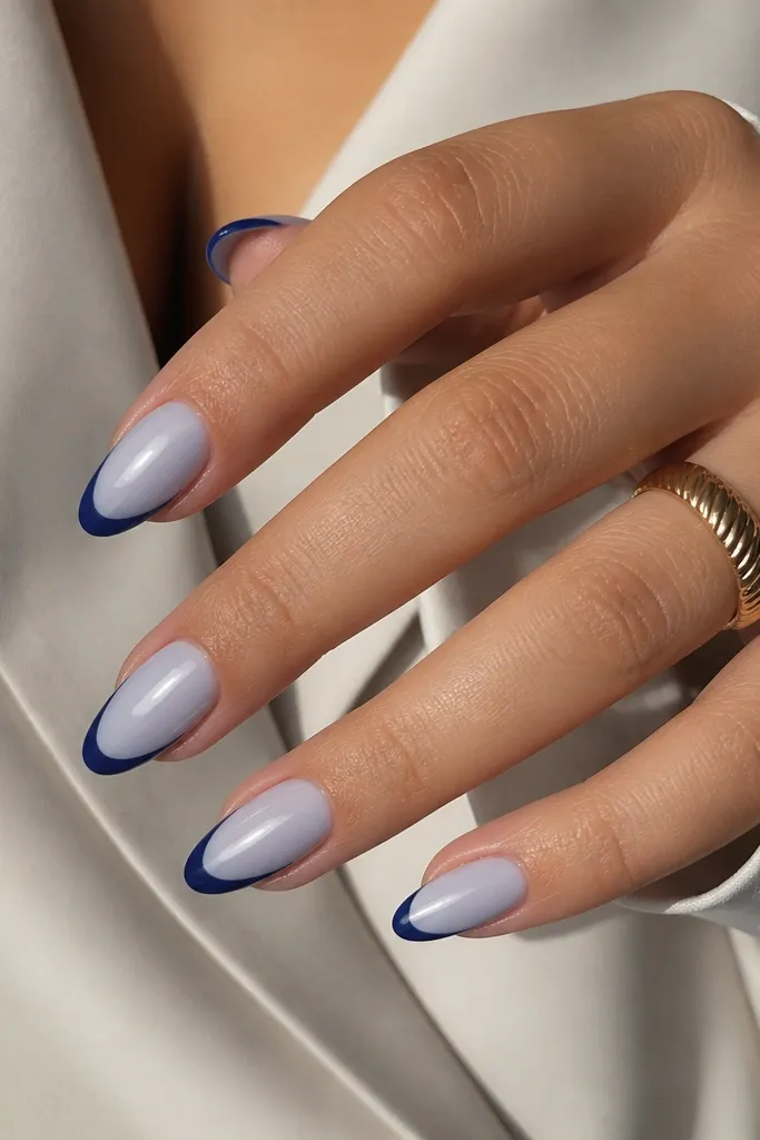 Medium almond nails with a nude base that has a slight blue tint, and navy French tips with a very smooth color match, glossy finish.
