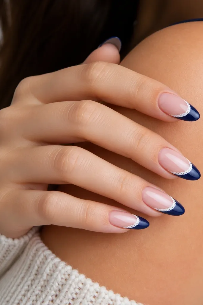 Almond nails with navy French tips and a white lace-like scalloped curve on the inner edge of the blue, glossy finish.