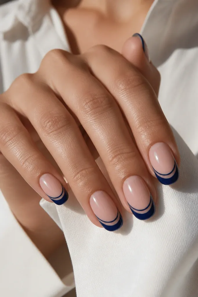 Nude base nails with a bold navy French that leaves a clear negative-space smile line in the center, creating a cutout effect, glossy finish.