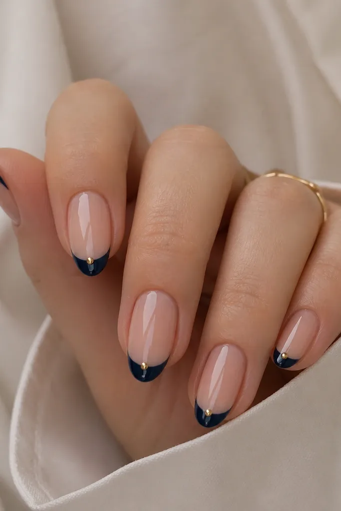 Medium almond nails with navy French tips and a single tiny gold stud centered at the very tip edge, glossy finish.