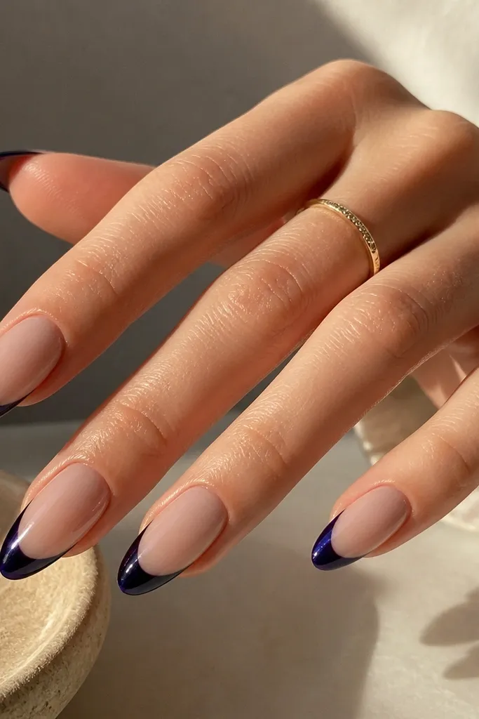 Almond nails with deep navy French tips that show a subtle purple tint when light hits, nude base, glossy finish.